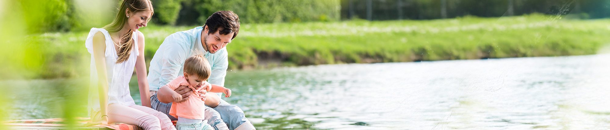 Mutter, Vater und Kind sitzen an einem See